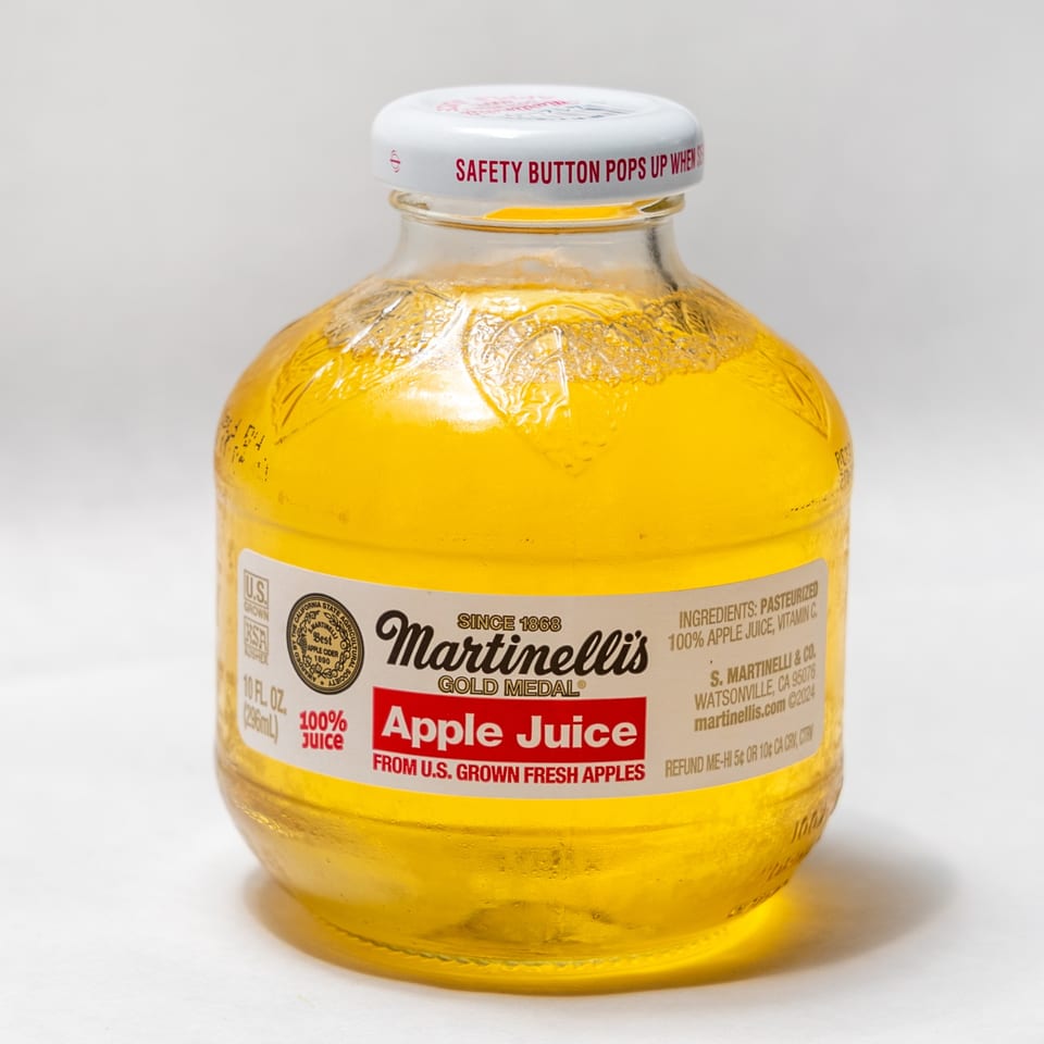 A clear glass bottle of Martinelli's Gold Medal apple juice with a white cap.
