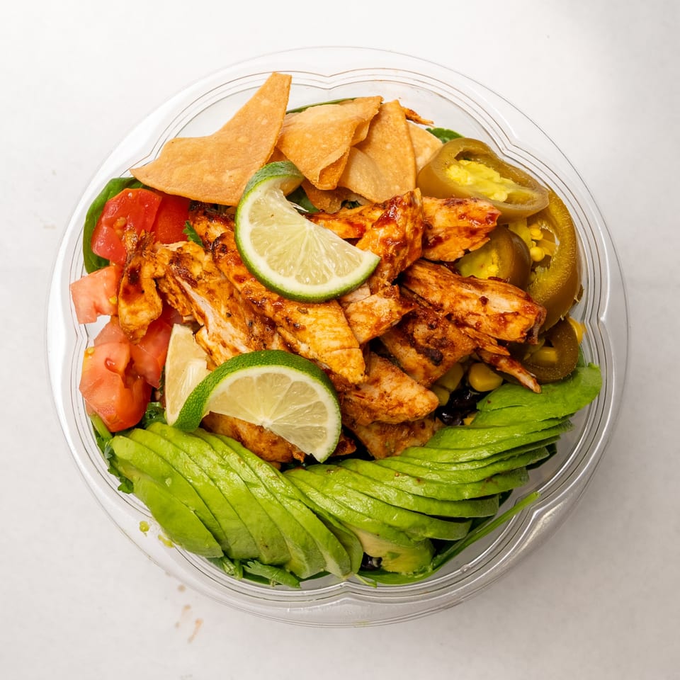 Overhead view of a vibrant salad with grilled chicken, avocado, tomatoes, tortilla chips, and limes.