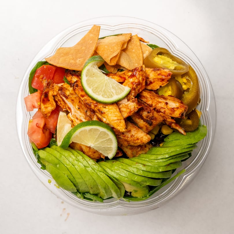 Overhead view of a vibrant salad with grilled chicken, avocado, tomatoes, tortilla chips, and limes.