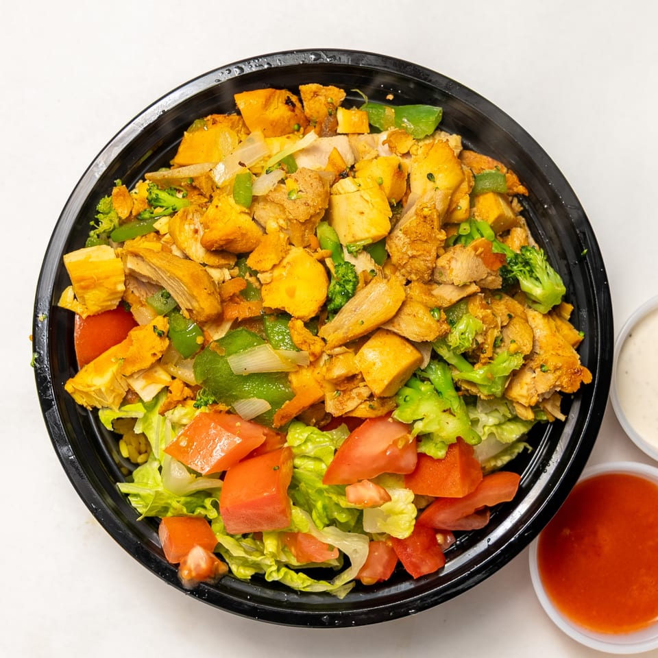 Chicken and vegetable bowl with lettuce, tomatoes, broccoli, and peppers, with two sauces on the side.