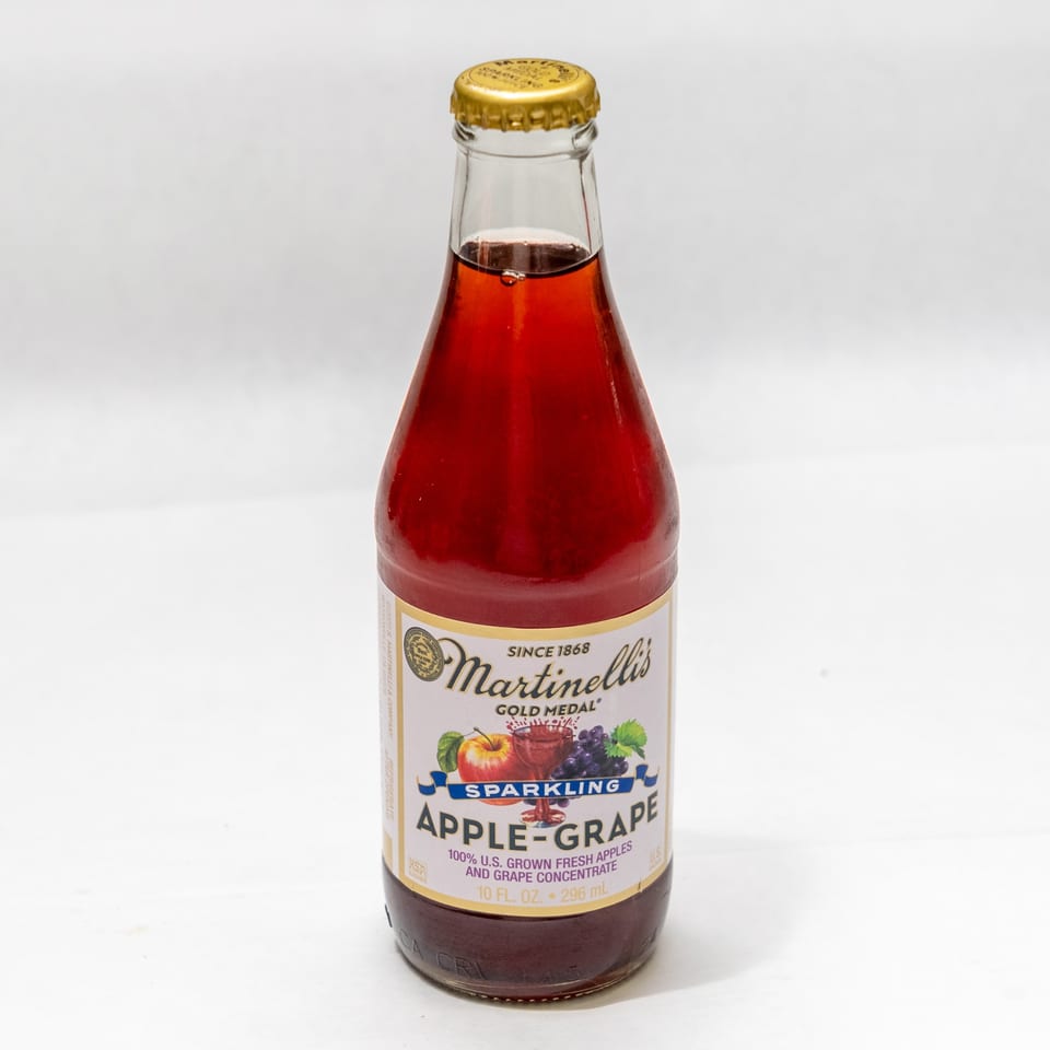 A bottle of Martinelli's Sparkling Apple-Grape juice with a gold cap on a white background.