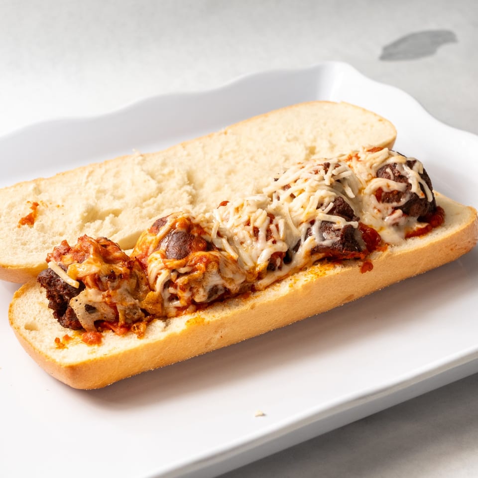 Meatball sub sandwich with melted cheese and marinara sauce on a white plate.