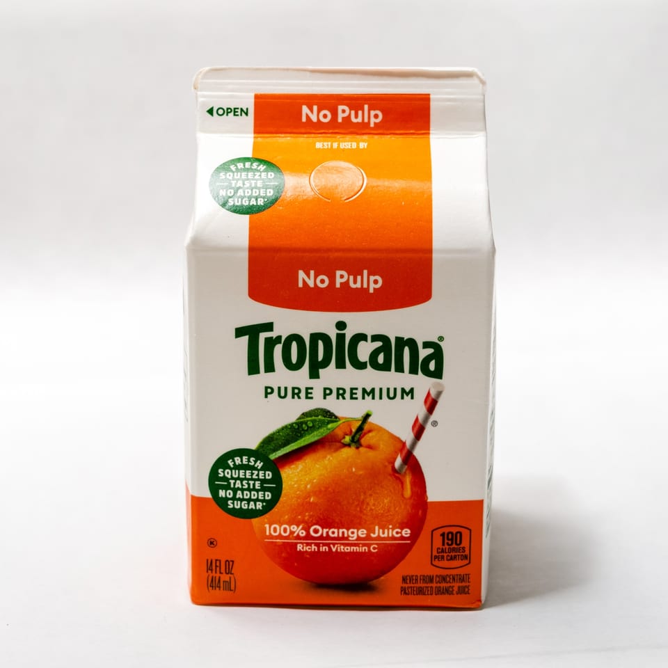 A white and orange Tropicana Pure Premium No Pulp orange juice carton with an orange and a straw.