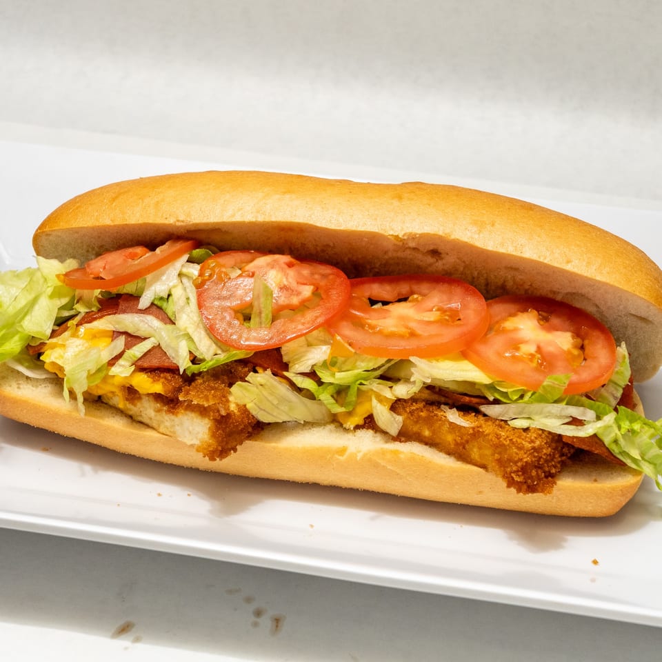 A crispy chicken sandwich on a sub roll with lettuce, tomatoes, bacon, and cheese.